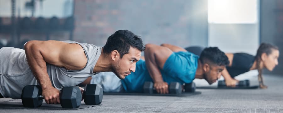 Two men performing push-ups with dumbbells during a strength-training workout at a gym