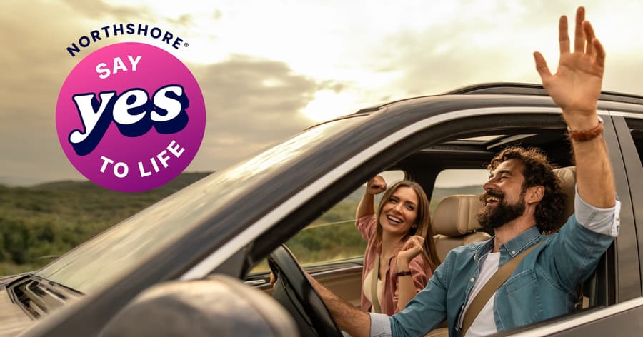 Smiling man and woman enjoying a drive with their arms raised, alongside the NorthShore “Say Yes to Life” logo.