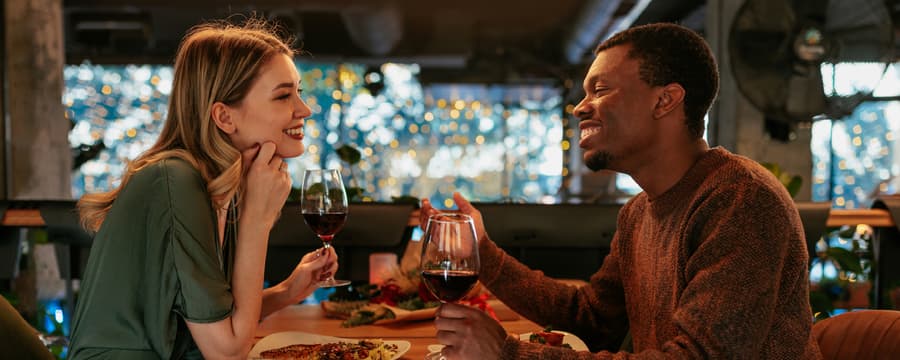 A smiling couple shares wine and conversation over dinner at a warmly lit restaurant.