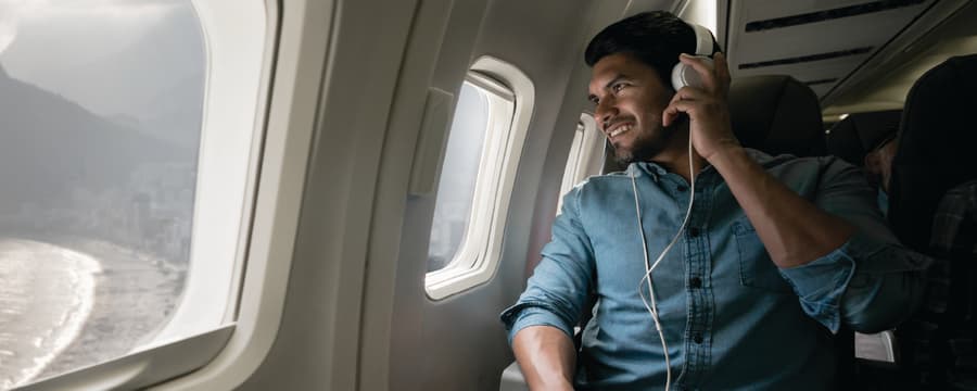 A man wearing headphones smiles while looking out the window of an airplane during a flight.