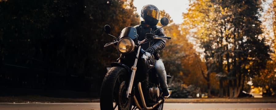Motorcyclist in black leather gear and helmet on a black motorcycle riding through a scenic autumn forest road