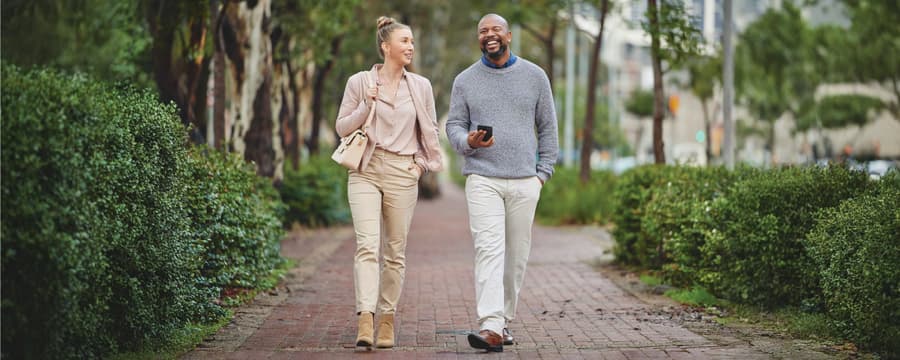 Man and woman smiling and talking while walking together along a tree-lined brick path.