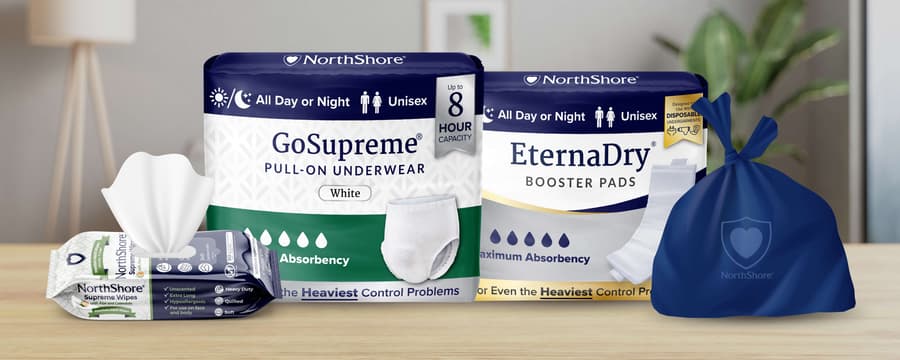 NorthShore incontinence essentials including GoSupreme pull-on underwear, EternaDry booster pads, Supreme Wipes, and disposal bag displayed on a table.