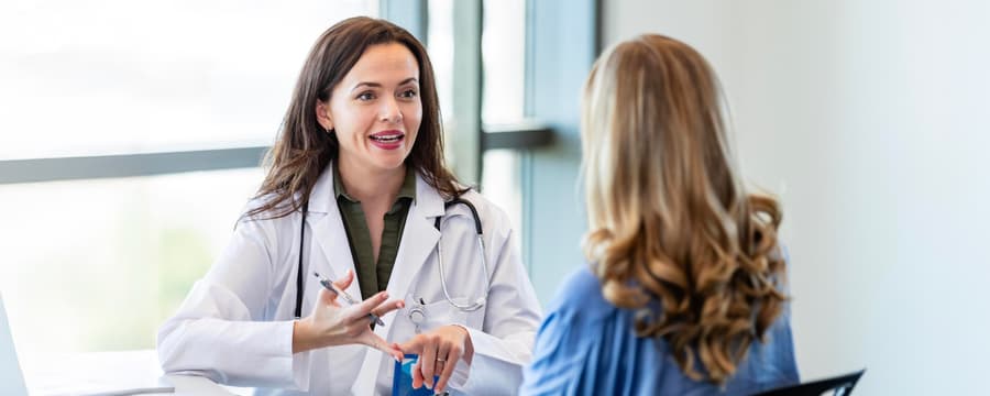 Female doctor in white coat talking to a female patient in a medical office, representing open healthcare communication.