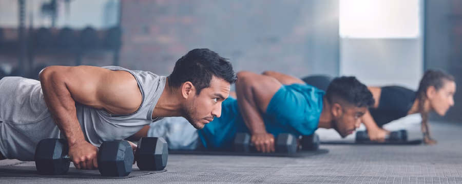 Two men performing push-ups with dumbbells during a strength-training workout at a gym