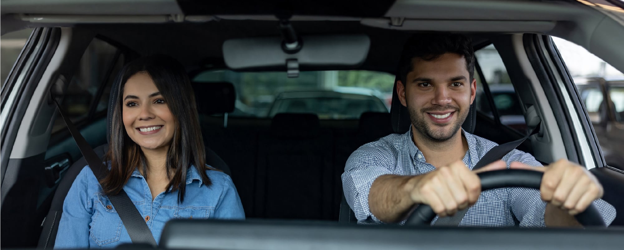 Smiling couple wearing seat belts while traveling together in a car.