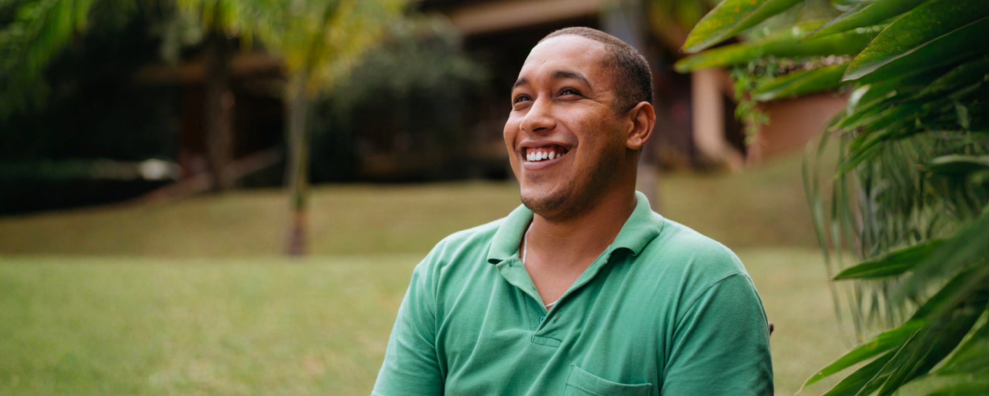 Smiling man in a green polo shirt sitting outdoors in a lush garden.