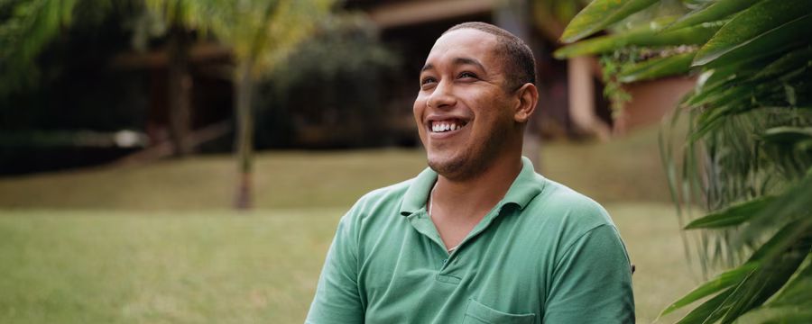 Smiling man in a green polo shirt sitting outdoors in a lush garden.