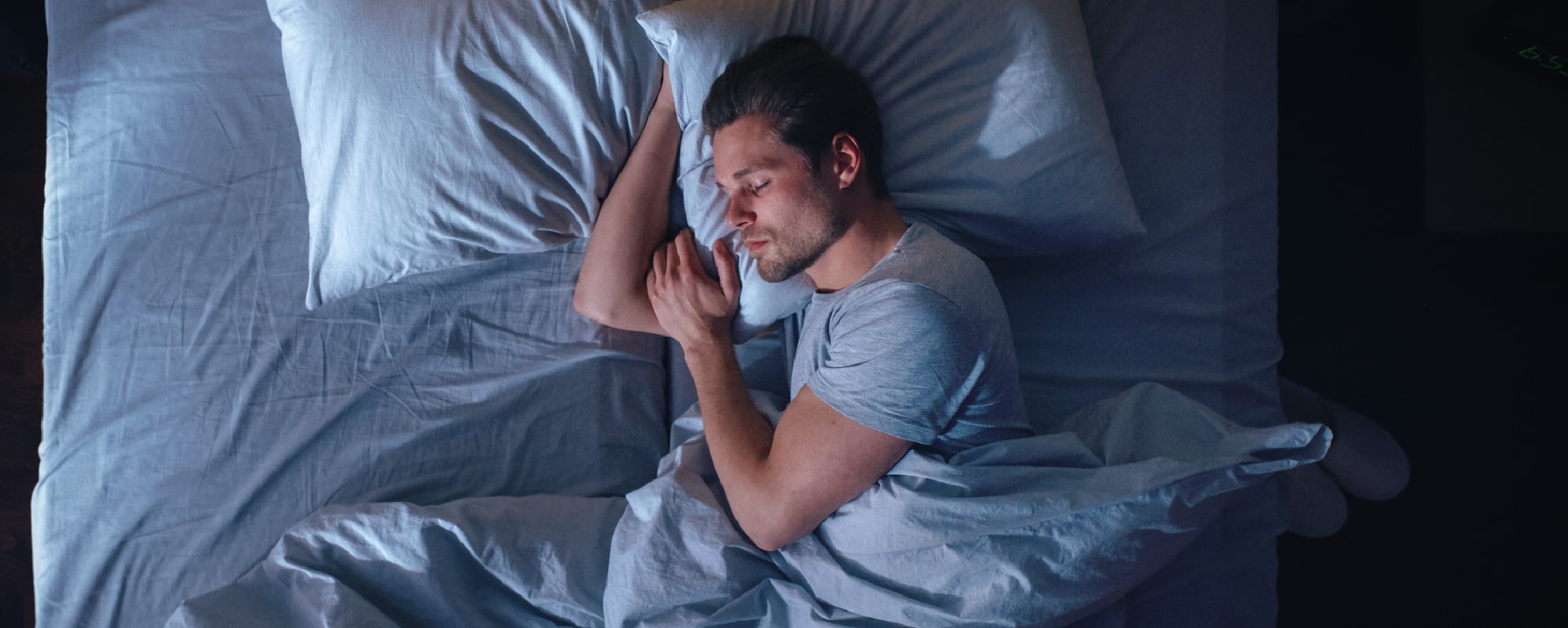 Man sleeping peacefully on his side in bed under blue-gray sheets.