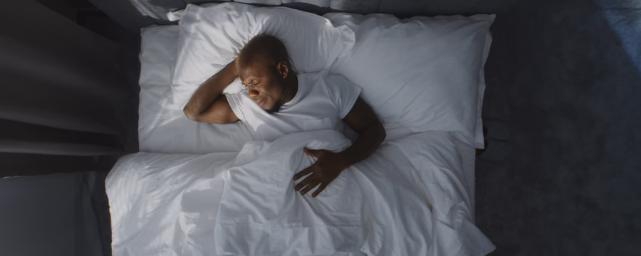 Man sleeping peacefully in bed under white bedding, viewed from above.