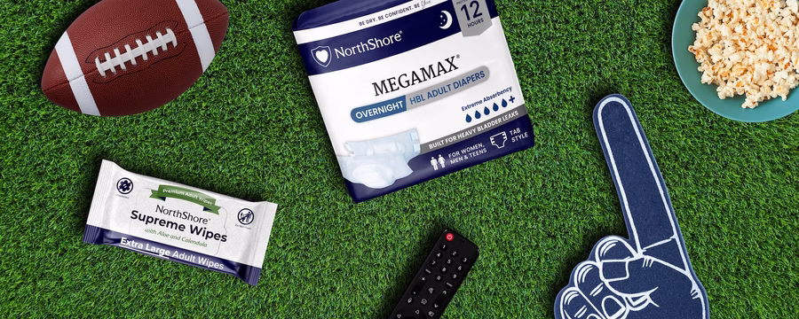 NorthShore MegaMax overnight adult diapers and Supreme Wipes arranged on artificial turf with a football, popcorn, TV remote, and foam finger.