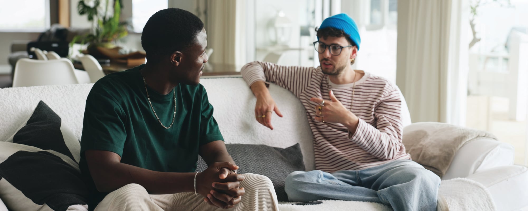 Two men sitting on a couch, engaged in conversation in a bright living room.