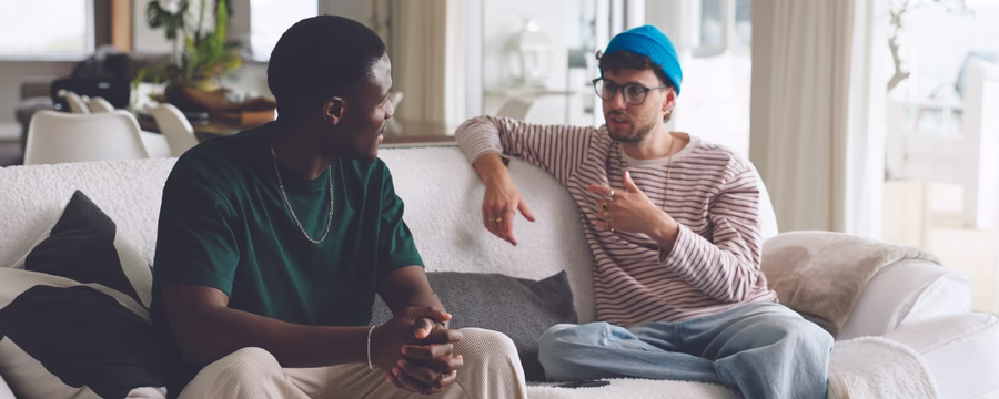 Two men sitting on a couch, engaged in conversation in a bright living room.