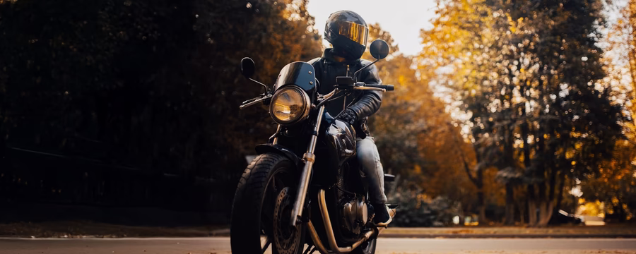 Motorcyclist in black leather gear and helmet on a black motorcycle riding through a scenic autumn forest road