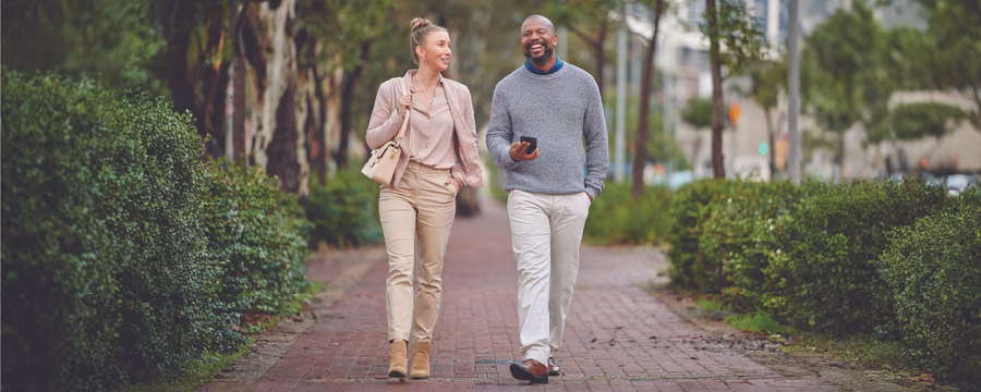 Man and woman smiling and talking while walking together along a tree-lined brick path.