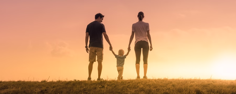Silhouetted parents walking hand-in-hand with their child during sunset on a grassy hill, symbolizing love, support, and togetherness.
