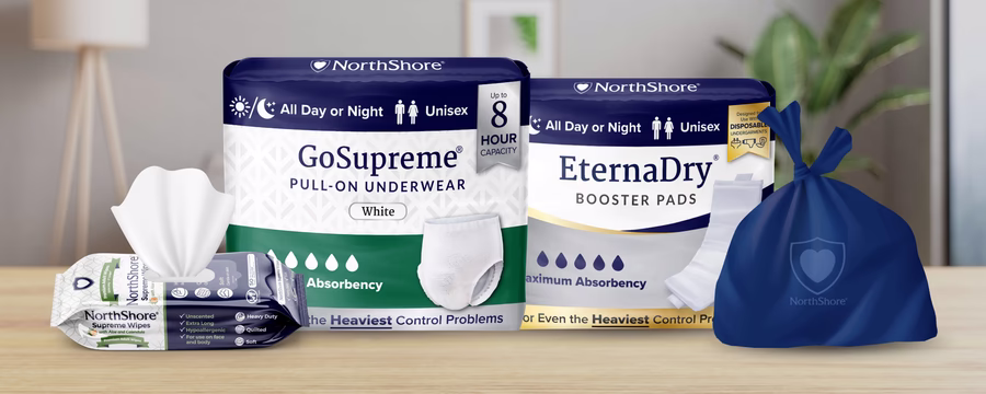 NorthShore incontinence essentials including GoSupreme pull-on underwear, EternaDry booster pads, Supreme Wipes, and disposal bag displayed on a table.