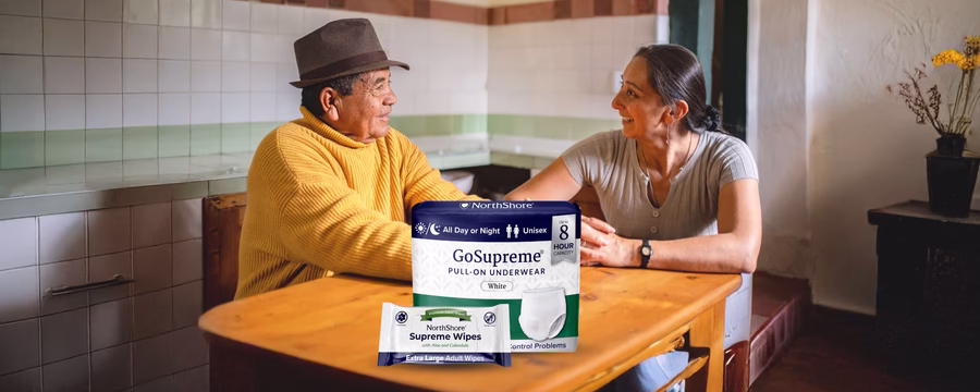 Elderly man and woman smiling at a table with NorthShore GoSupreme underwear and Supreme Wipes, representing real-world caregiving solutions