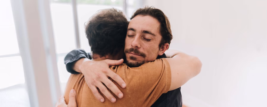 Two men hugging in a bright room, symbolizing emotional support and connection for those managing incontinence