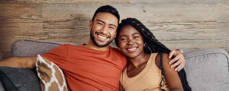 Smiling couple sitting close together on a couch, showing comfort, trust, and support in relationships