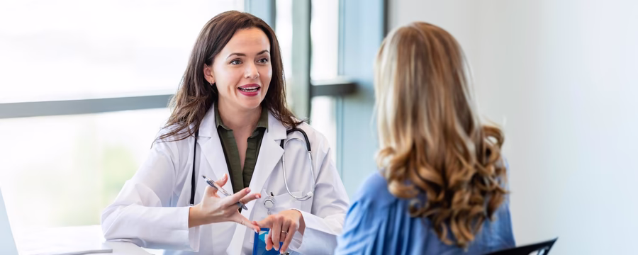 Female doctor in white coat talking to a female patient in a medical office, representing open healthcare communication.