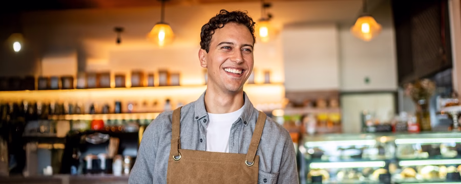 Smiling male barista in an apron inside a café, conveying confidence and everyday work life.