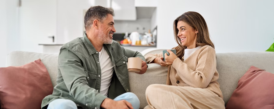 Middle-aged couple sitting on a couch enjoying coffee and conversation, highlighting healthy relationships and communication.