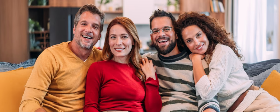 Four friends sitting close together indoors, smiling and enjoying time together, representing community and emotional support.