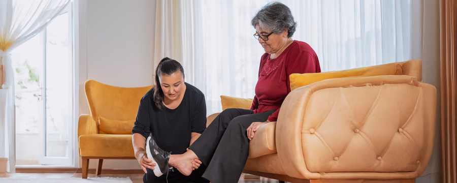 Caregiver helping an older woman put on a shoe, highlighting compassionate in-home support for seniors.