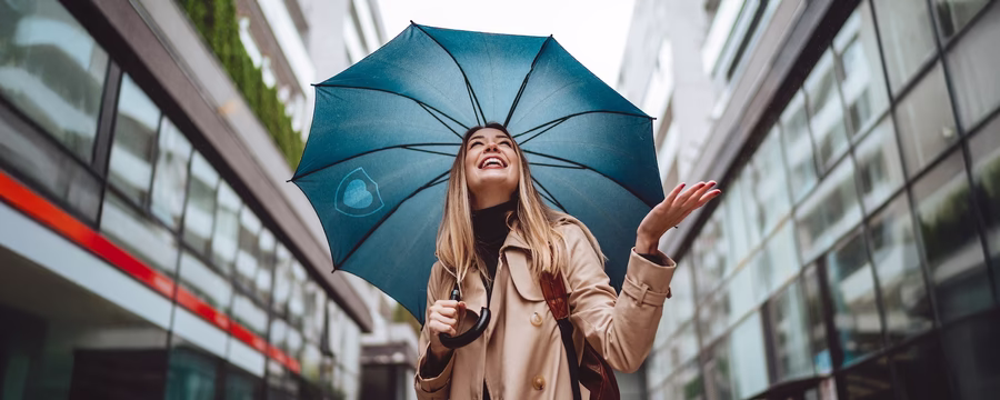 Happy woman holding a blue umbrella and smiling in the rain, symbolizing finding real protection from incontinence leaks.